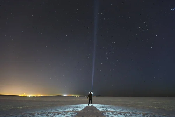 Silhuetten av en man med en ficklampa, observerar vackra, breda blå natthimmel med stjärnor och synliga Vintergatan. Astronomi, orientering, klar himmel koncept och bakgrund. Stockbild