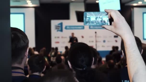 Un hombre toma una foto por teléfono móvil en una reunión de negocios, seminario o conferencia — Vídeo de stock