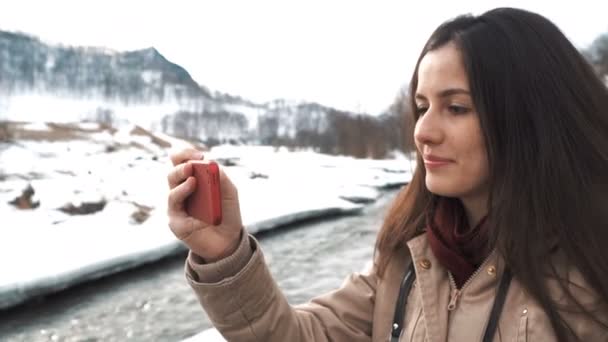 Hermosa mujer caucásica tomando selfie contra el fondo de grandes montañas y río de montaña verde — Vídeos de Stock