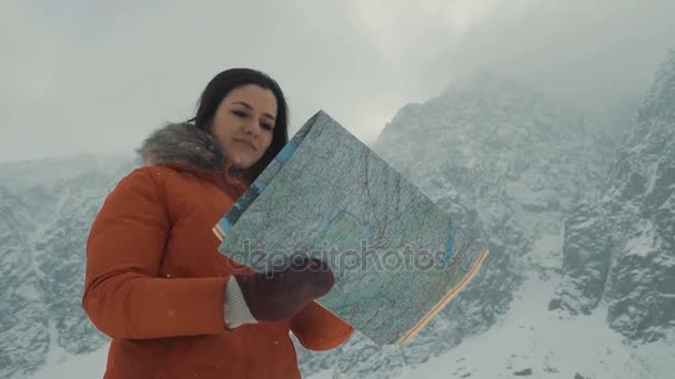 Девушка изучает карту на фоне заснеженных гор — стоковое видео