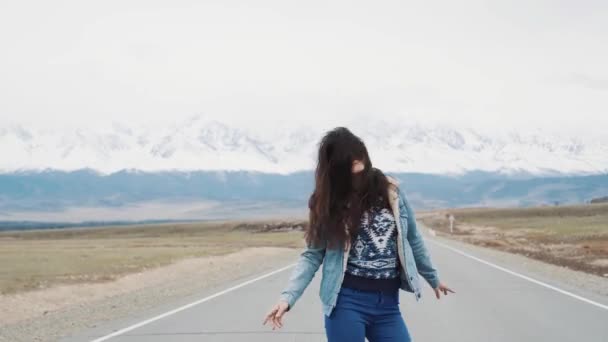 Linda menina adolescente hipster dançando na estrada contra o pano de fundo das montanhas. Estou feliz e feliz. Jaqueta de jeans e morena — Vídeo de Stock