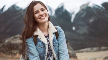 Genç kız Gezgin dağlar, kameraya gülümseyen manzarayı kayanın üzerinde oturur