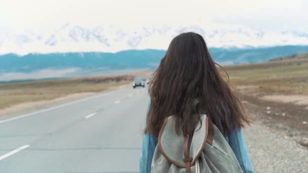 Jonge vrouw kink in de kabel-wandelen op een weg bij de velden. Jong meisje hippie liften op de weg. Tussen de bergen in de natuur. Gaan op de weg. — Stockvideo