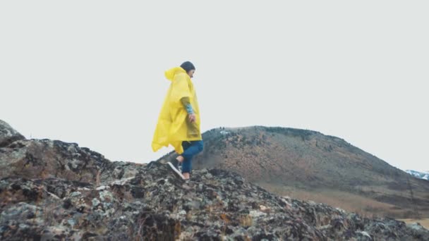 Kuray Ρωσία - 01.05.2017: Ένα νεαρό κορίτσι σε ένα κίτρινο μανδύα πηγαίνει και τρέχει κατά μήκος των βράχων. Ένας ταξιδιώτης ταξιδεύει ανάμεσα στα βουνά. — Αρχείο Βίντεο