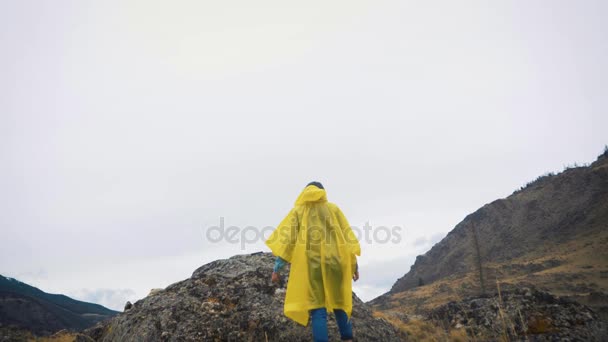 Kuray Ryssland - 01.05.2017: En ung flicka i en gul mantel går och löper längs klipporna. En resenär reser bland bergen. — Stockvideo