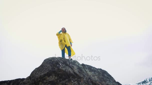 Ένα νεαρό κορίτσι σε ένα κίτρινο μανδύα πηγαίνει και τρέχει κατά μήκος των βράχων. Ένας ταξιδιώτης ταξιδεύει ανάμεσα στα βουνά. — Αρχείο Βίντεο