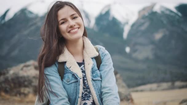 Young girl traveler sits on the rock, enjoying the view of the mountains, smiling at the camera — Stock Video