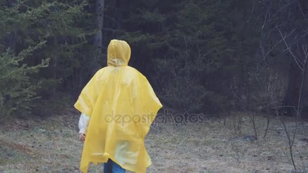 Мандрівник одягнений у жовтий плащ. Вид ззаду молодої жінки-хокеїстки під час походу з рюкзаком через густу лісову природу. Молода дівчина живе активним способом життя — стокове відео