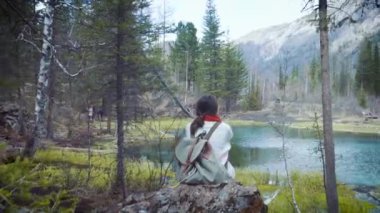 Mutlu kız Gezgin kayanın üzerinde oturur, bir dağ krater Gölü görünüyor. Bir kot ceket yürüyüş ve sırt çantası hiking giyinmiş. Yalnız, kendinizi bulma seyahat