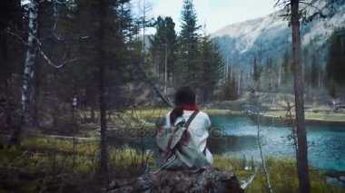 Mutlu kız Gezgin kayanın üzerinde oturur, bir dağ krater Gölü görünüyor. Bir kot ceket yürüyüş ve sırt çantası hiking giyinmiş. Yalnız, kendinizi bulma seyahat