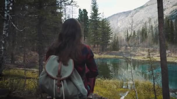 Happy girl traveler senta-se na rocha, faz uma foto no lago cratera de montanha smartphone. Vestida com um casaco de jeans e mochila para caminhadas. Viaje sozinho, encontrando-se . — Vídeo de Stock
