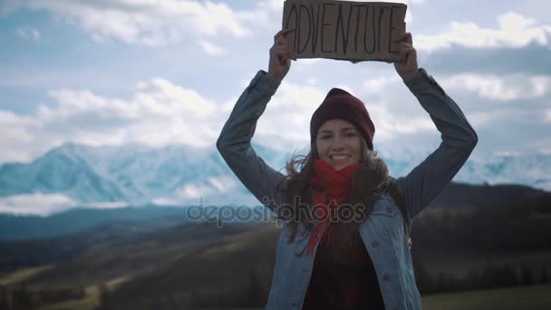 Ragazza adolescente che tiene un segno di avventura su una strada di montagna, sorrisi e risate — Video Stock