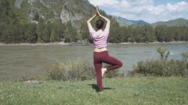 Genç güzel kadın kırmızı tank top açık havada, pratik bükme ağaç duruş, Vrksasana, Park yaz gününde varyasyonu yapıyor. Altay, nehir katun.