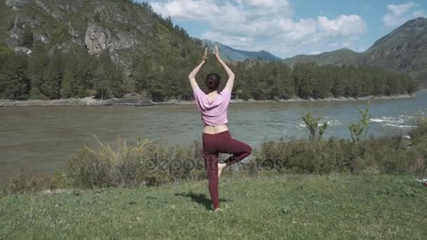Joven mujer hermosa en camiseta roja practicando al aire libre, haciendo la postura del árbol de flexión, variación de Vrksasana, en el parque en el día de verano. Altai, el río Katún . — Vídeos de Stock