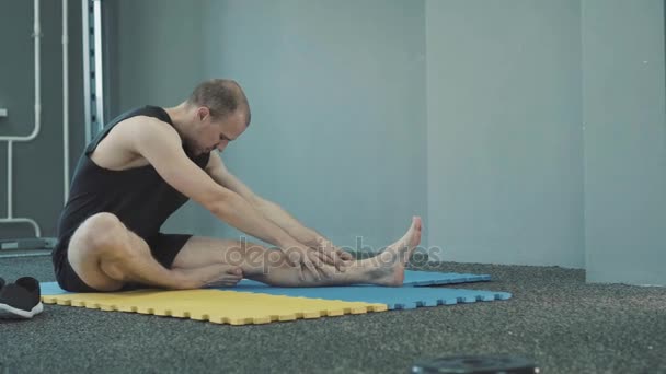 Férfi keres komoly stretching, és egy kék sárga Matt néhány testmozgás bemelegítés közben — Stock videók