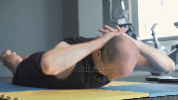 Чоловік виглядає серйозно, розтягуючись і розігріваючись на синьо-жовтому килимку для деяких вправ — стокове відео