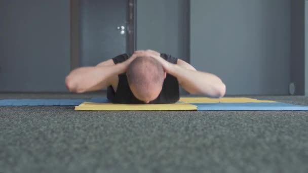 Homme à l'air sérieux tout en s'étirant et se réchauffant sur un tapis bleu jaune pour un peu d'exercice — Video