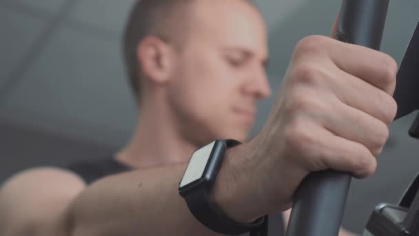 Jovem com smartwatch andar de bicicleta estacionária no ginásio — Vídeo de Stock