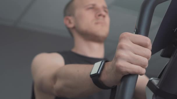 Hombre joven con smartwatch montar bicicleta estacionaria en el gimnasio — Vídeos de Stock