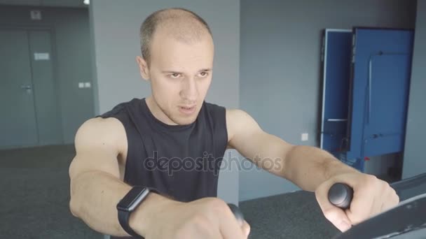 Młody człowiek z zegarka smartwatch, jazda konna, jazda na rowerze stacjonarnym w siłowni — Wideo stockowe