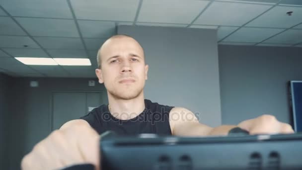 Mladý atraktivní muž na kole na rotopedu v tělocvičně — Stock video