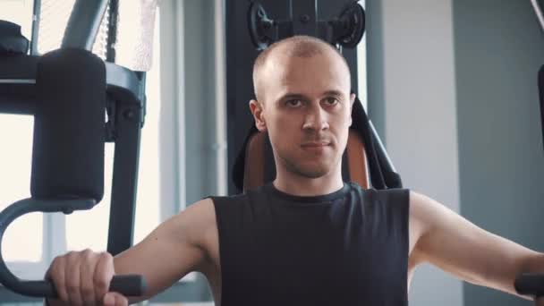 Молодий м'язистий чоловік тренування жорсткий на веслувальній машині у фітнес студії — стокове відео