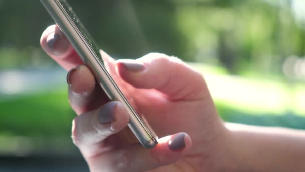 Primeros planos de manos femeninas Use un teléfono inteligente, pulsando a través de la información en la pantalla táctil. la pantalla del teléfono refleja la luz del sol . — Vídeos de Stock
