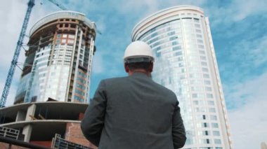 Yetişkin mühendis veya mimar bir tablet işlemi kullanır. Bir ileti yazar veya bir çizim denetler. Arka planı yapıdır. İnşaatçılar beton ve cam modern konut bina inşa ediyoruz