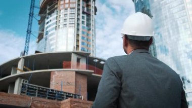 Yetişkin mühendis veya mimar bir tablet işlemi kullanır. Bir ileti yazar veya bir çizim denetler. Arka planı yapıdır. İnşaatçılar beton ve cam modern konut bina inşa ediyoruz