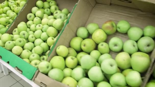 Девушка в супермаркете выбирает зеленые яблоки. Женщина вручную выбирает и покупает зеленые яблоки в супермаркете. Большая куча зеленых яблок в коробках — стоковое видео