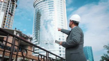 Yetişkin mühendis veya mimar bir tablet işlemi kullanır. Bir ileti yazar veya bir çizim denetler. Arka planı yapıdır. İnşaatçılar beton ve cam modern konut bina inşa ediyoruz