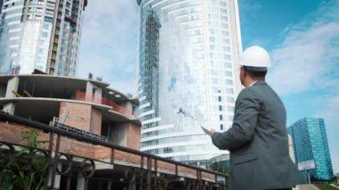 Yetişkin mühendis veya mimar bir tablet işlemi kullanır. Bir ileti yazar veya bir çizim denetler. Arka planı yapıdır. İnşaatçılar beton ve cam modern konut bina inşa ediyoruz