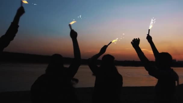 Zpětná přátelé běží spolu na pláži drží šumivé ohňostroj. přítelkyně přítelkyně běžet podél pobřeží, večer nebo v noci — Stock video