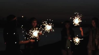 Dikiz parlak havai fişek tutan bir kumsalda birlikte çalışan arkadaşlar. kız kız akşam veya gece kıyıya çalıştırmak