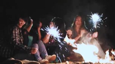 Sahilde akşamları ateşin ortasına gençlerle piknik. Şarkılar ve gitar çalmak neşeli arkadaşları. Ellerinde yanan Bengal ışıkları tutun.