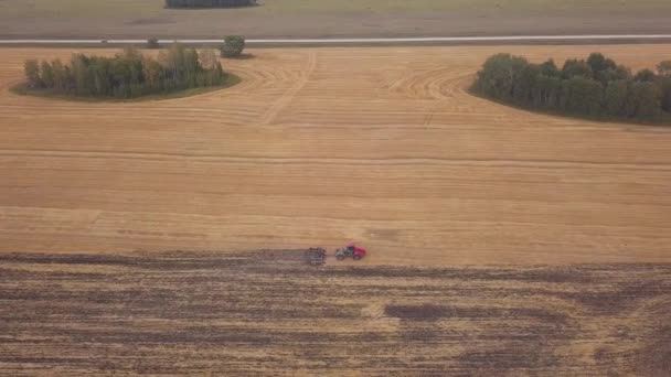AERIAL: стрілянина в безпілотник над полем орної землі. Червоний трактор розчищає поле восени — стокове відео