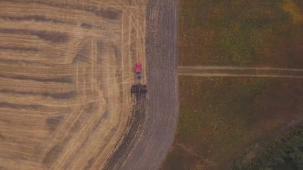 AERIAL: disparando al dron sobre el campo de tierra cultivable. Un tractor rojo despeja el campo en el otoño — Vídeo de stock