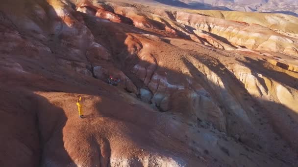 Aereo: Una giovane ragazza in piedi su una montagna rossa che fa volare il suo aquilone in alta montagna sullo sfondo. l'idea di libertà, la ricerca di avventure in montagna. La ragazza sogna un più grande . — Video Stock