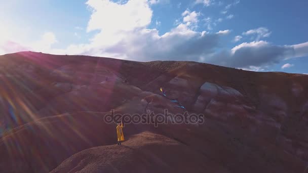 Aerial: A young girl standing in red mountain flying her kite in high mountains on background. the idea of freedom, the search for adventures in the mountains. The girl dreams of a greater. — Stock Video