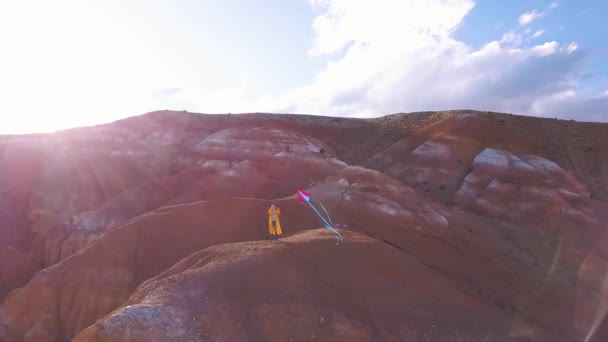 航空: 背景に高山で彼女の凧を飛ぶ赤い山に立っている若い女の子。自由、山での冒険の検索のアイデア。大きいの女の子の夢. — ストック動画