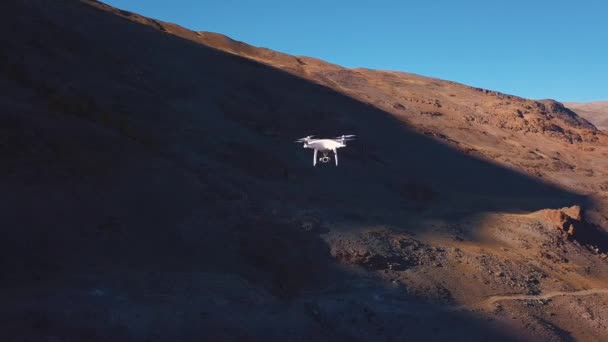 Drohnenflug in der Schlucht, in einer Luftaufnahme. Ein weißer großer Quadrocopter oder eine Drohne fliegt zwischen den Gipfeln der Berge hin und her. Flug mit einer Drehung. entfernt die Beschaffenheit der Videokamera — Stockvideo