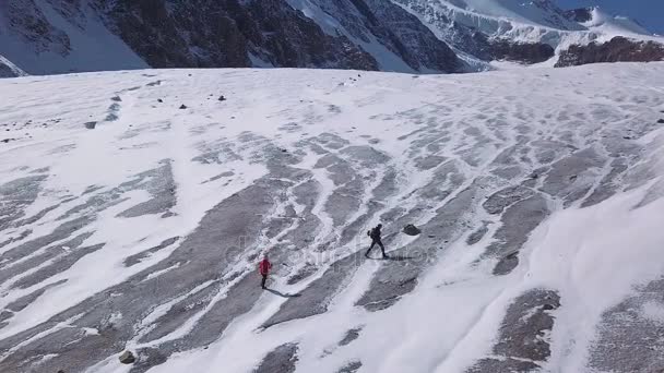 Aéreo: Um homem e uma mulher escalam a geleira para uma alta montanha no Alasca. Caminhantes profissionais estão envolvidos em caminhadas — Vídeo de Stock