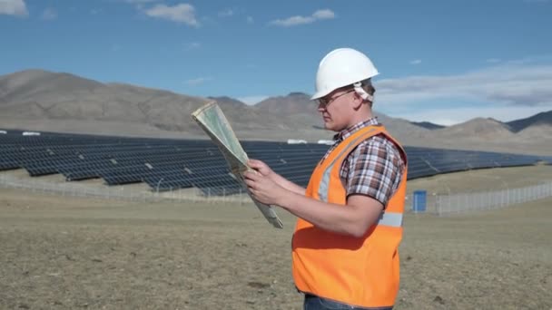 Engineer in a helmet and vest working on a project of solar panels in the desert. — Stock Video