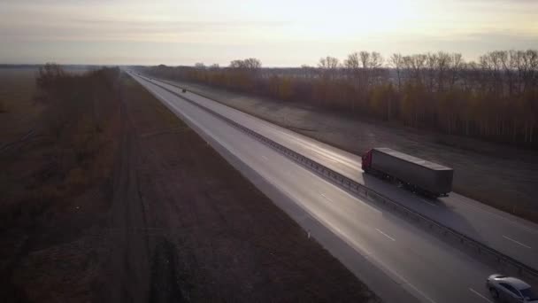 AERIAL: Delivery trucks driving towards the sun. the car with the container rides on the road to the sunset. Truck rides the highway. — Stock Video