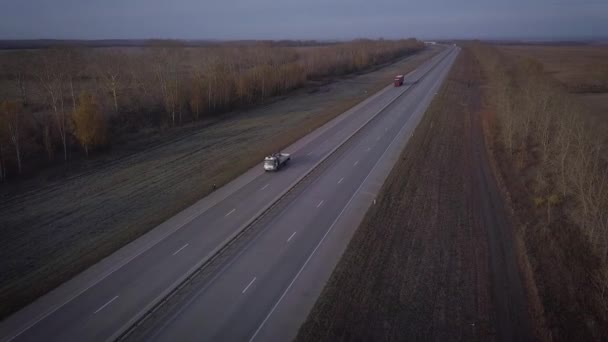 AERIAL: Delivery trucks driving towards the sun. the car with the container rides on the road to the sunset. Truck rides the highway. — Stock Video