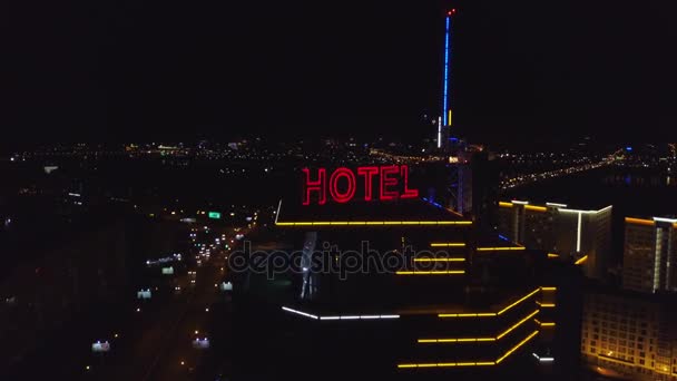 Κεραία: Ξενοδοχείο Neon κόκκινη επιγραφή στη στέγη του ένα σύγχρονο κτίριο της πόλης το βράδυ. Αυτοκίνητα της κυκλοφορίας είναι δίπλα στο δρόμο. Το ξενοδοχείο λέξη στη στέγη ενός ουρανοξύστη — Αρχείο Βίντεο