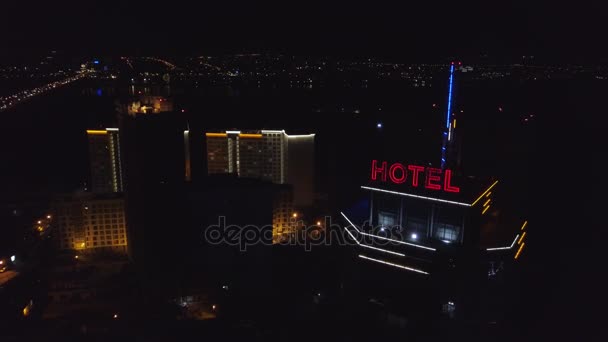 AÉRIAL : Hôtel inscription rouge fluo sur le toit d'un bâtiment moderne dans la ville nocturne. Les voitures de circulation sont les prochaines sur la route. Le mot hôtel sur le toit d'un gratte-ciel — Video