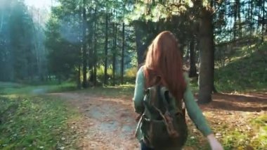 Bir sırt çantası ile genç bir güzel kızıl saçlı kız bir orman veya park üzerinden yürüyor. Yalnız, hipster walker seyahat