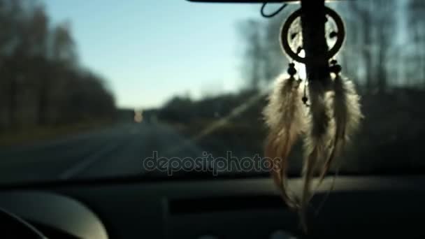 Vue du capteur de rêves suspendu depuis le rétroviseur intérieur de la voiture. Voyagez en voiture. Vue sur la route et les montagnes enneigées le soir . — Video