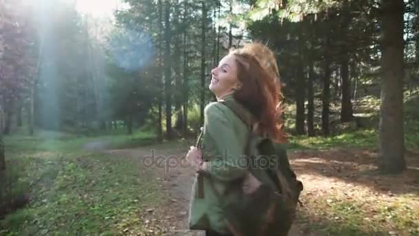 Молода красива руда дівчина з рюкзаком проходить через ліс або парк. Подорожуйте один, хіпстер ходить — стокове відео